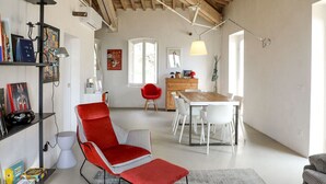 A spacious living area with a red armchair, a dining table with white chairs, and a kitchen in the background. - For those who love to pause in history and stories (Assisi)