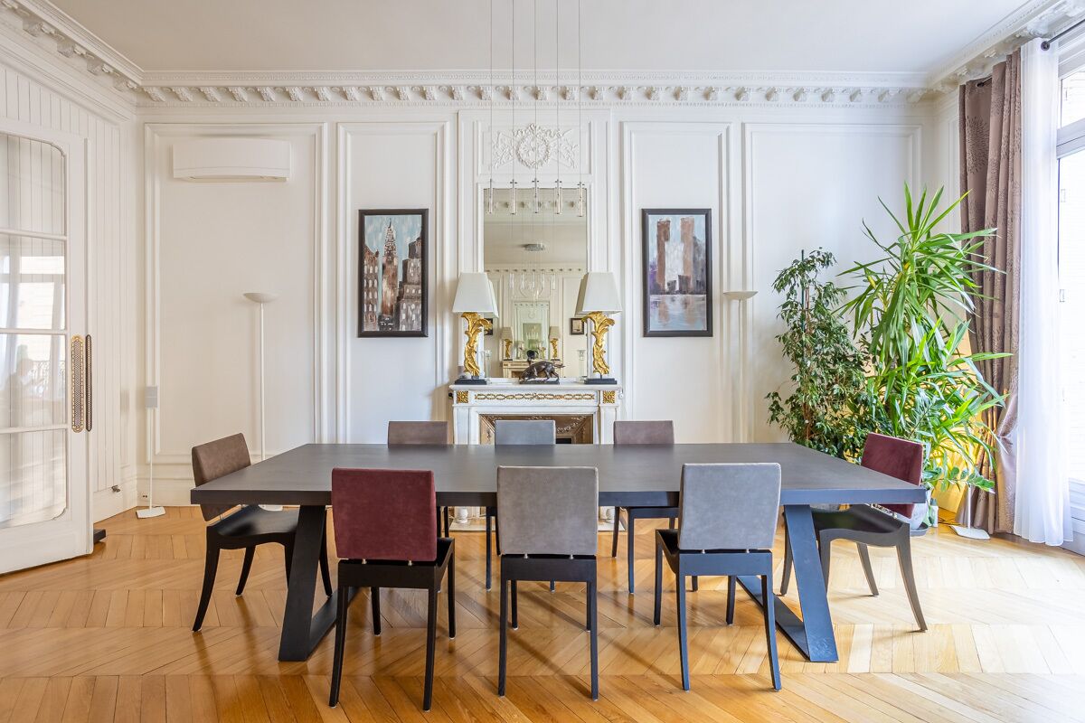 A dining room with a long table, multiple chairs, a fireplace, and framed artwork on the walls.