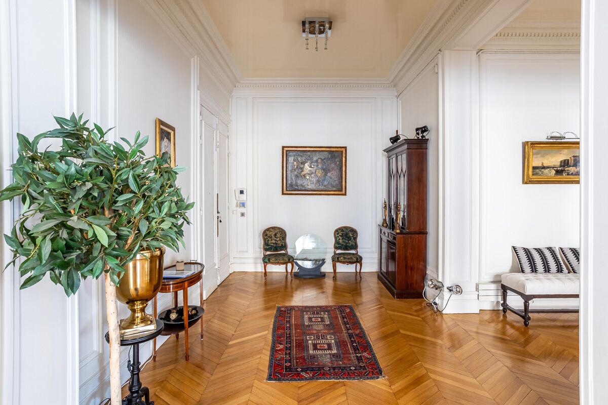 A room with a wooden floor, a large green plant, two chairs, a sofa, and a painting on the wall.