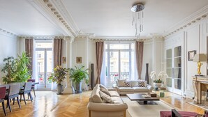 Ein geräumiges Wohnzimmer mit Holzboden, einer Sofagarnitur, einem Esstisch mit Stühlen und Topfpflanzen.