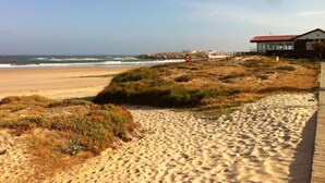 A sandy beach with a wooden boardwalk leading to a building with a red roof. - Apartment with open views to the Atlantic Ocean (Foz do Arelho)
