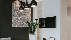 A modern living room with a grey sofa, a wooden coffee table, a potted plant, a white entertainment unit, and a mounted TV. - Mia Apartments (Kraków)