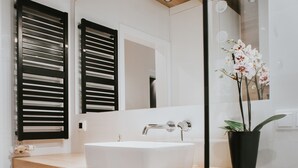 A modern bathroom with a white sink, wooden vanity, black shutters, a potted orchid, and a mirror reflecting the room. - Mia Apartments (Kraków)