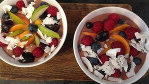 Two bowls of fruit salad with a variety of berries and sliced fruits on a wooden board. - Mia Apartments (Kraków)