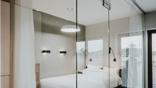 A modern bedroom with a glass partition, a large bed, and a city view. - Mia Apartments (Kraków)