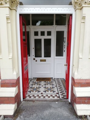 A white door with a red frame, a doormat, and a patterned tile floor. - Luxury Holiday/Business Accommodation in Heart of West Kirby (West Kirby)