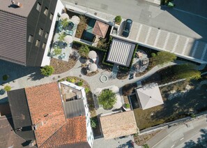 An aerial view of a residential area with a swimming pool, outdoor seating, and a modern building with a sloped roof. - Gasthaus Traube (Niederfell)