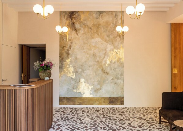 A reception area with a wooden reception desk, a large abstract painting on the wall, and a patterned floor. - Gasthaus Traube (Niederfell)