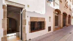 A narrow street with a building featuring a large open doorway, a barred window, and a tiled entrance.
