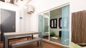 A small, modern room with a sliding glass door leading to a balcony, a wooden bench, and a small table.