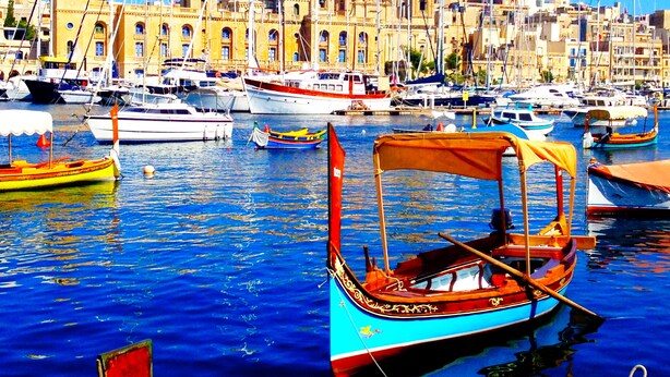 A harbor with boats, a prominent building with a clock tower, and a clear blue sky.