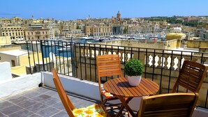 A balcony with a table and chairs, a potted plant, and a view of a marina and cityscape.