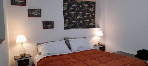Un dormitorio con una cama, dos lámparas de noche, una mesita de noche y una pared con tres cuadros enmarcados.