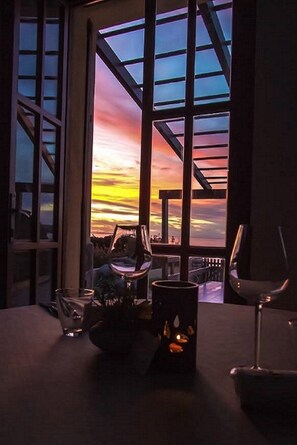 A table set with wine glasses and a candle, with a view of a sunset through a large window. - The cottage on the beach, 10 mt from the sea, private parking space  (San Vero Milis Oristano)