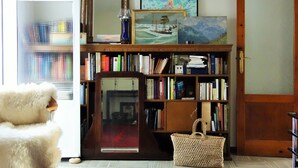 A room with a bookshelf, a mirror, a red rug, and a white chair.