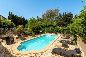 Ein rechteckiger Swimmingpool mit einer Steinumrandung, umgeben von Liegestühlen und einer Steinterrasse.
