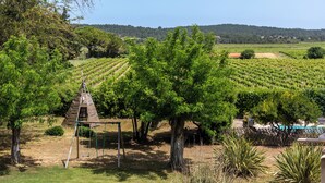 A vineyard with rows of grapevines, a wooden swing set, and a pool area. - Character gite with swimming pool, surrounded by vineyards, 30 min drive from the Mediterranean coast. (Fabrezan)