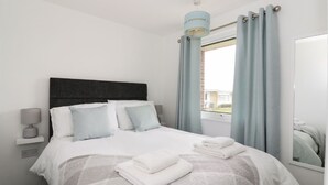 A modern bedroom with a large bed, a bedside table, a lamp, and a window with curtains. - 5* Light & Airy Chalet 5min walk 2 beach nr BroadsSunbeach Chalets 143 a contemp (Great Yarmouth)