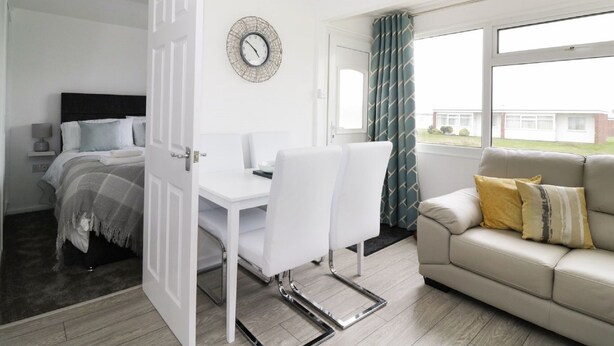 A modern bedroom with a bed, bedside table, and a clock on the wall. - 5* Light & Airy Chalet 5min walk 2 beach nr BroadsSunbeach Chalets 143 a contemp (Great Yarmouth)