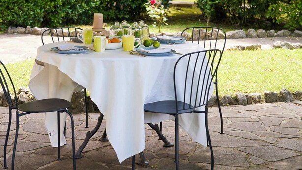 Une table dressée à l’extérieur, avec une nappe, des chaises et une lanterne suspendue.