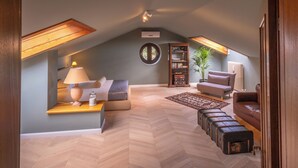 Une chambre mansardée chaleureuse, avec un lit en mezzanine, un fauteuil de lecture, une petite table avec une lampe, une bibliothèque et une plante en pot.