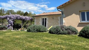 Una casa con fachada de piedra, techo de tejas y un jardín con un arco floral púrpura.