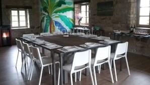 Ein Essbereich mit einem langen Tisch, gedeckt für 12 Personen, umgeben von weißen Stühlen. An der Wand hinter dem Tisch ist eine Wandmalerei von einer Palme zu sehen.