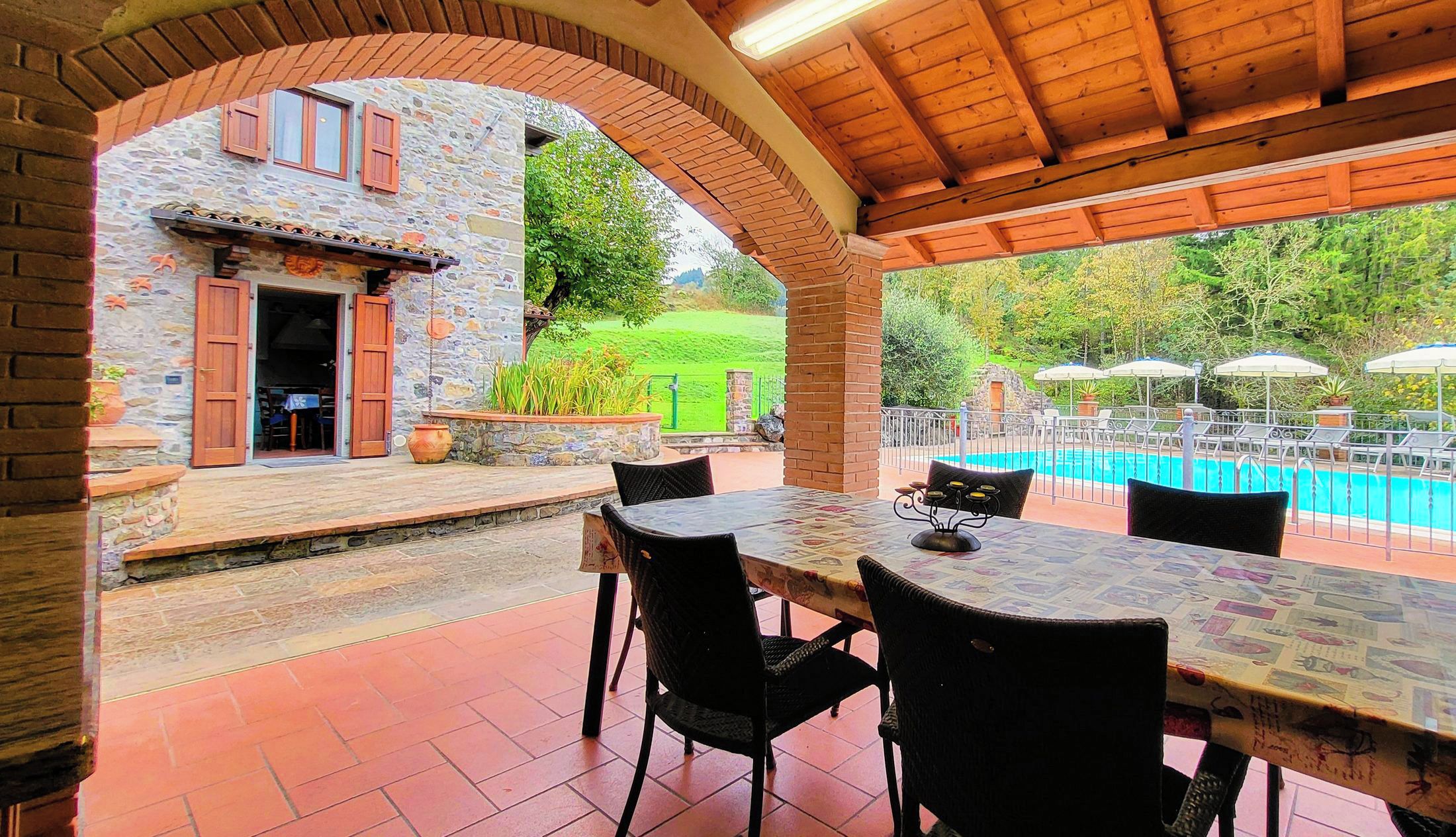 A covered outdoor area with a pool, stone walls, and outdoor seating.