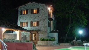 Un edificio in pietra con piscina, una zona riparata con panchina e un ingresso ben illuminato.