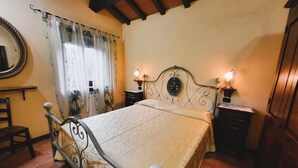 Une chambre à coucher avec un lit, une table de chevet, une lampe, un miroir et une fenêtre avec des rideaux.