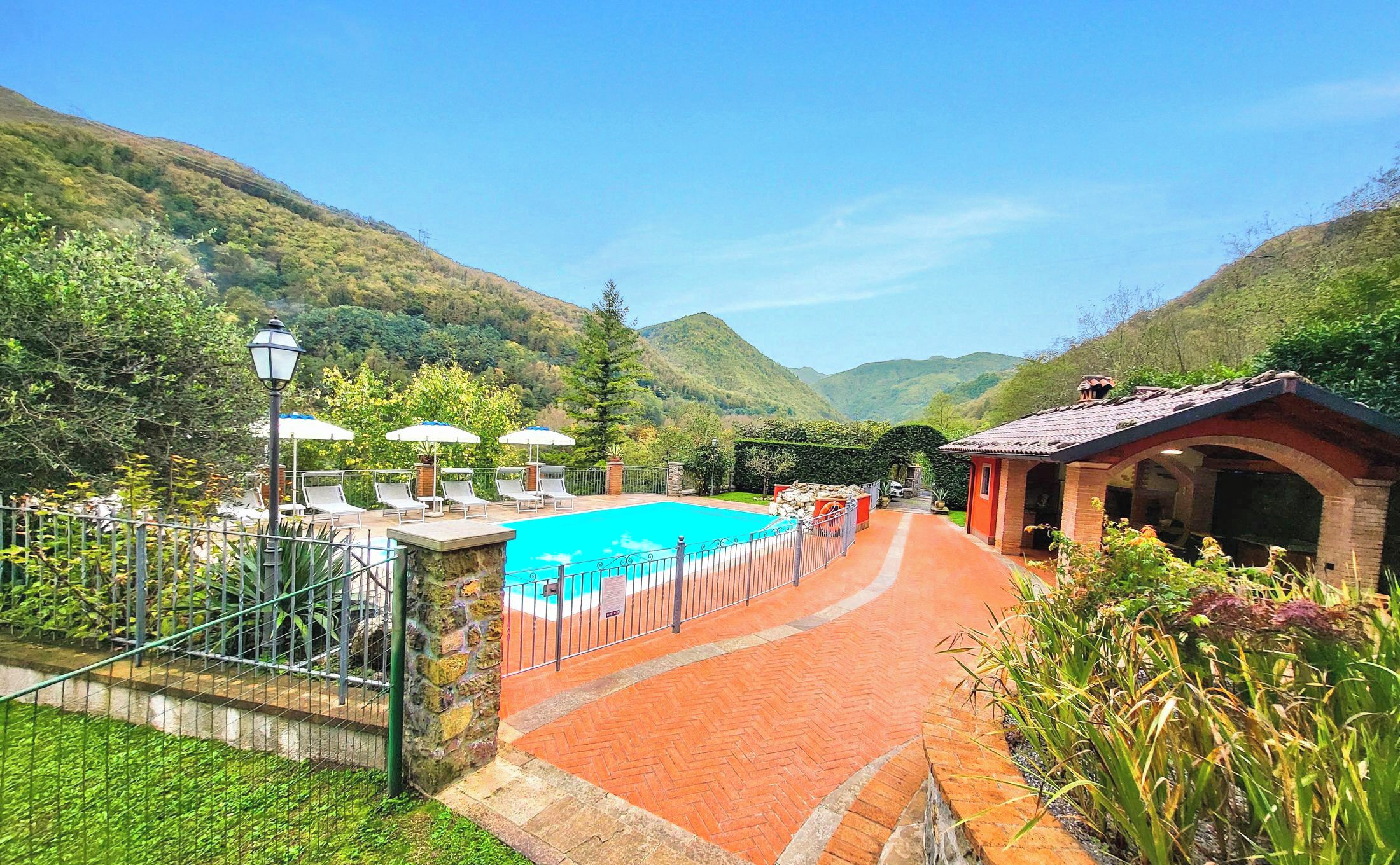 A pool area with a clear view of the mountains, a covered seating area, and a stone pathway leading to the pool.