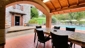 Une terrasse couverte avec une piscine, des murs en pierre et des sièges d’extérieur.