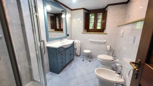 Un bagno con cabina doccia in vetro, un mobile lavabo blu con lavandino, un water e un bidet.