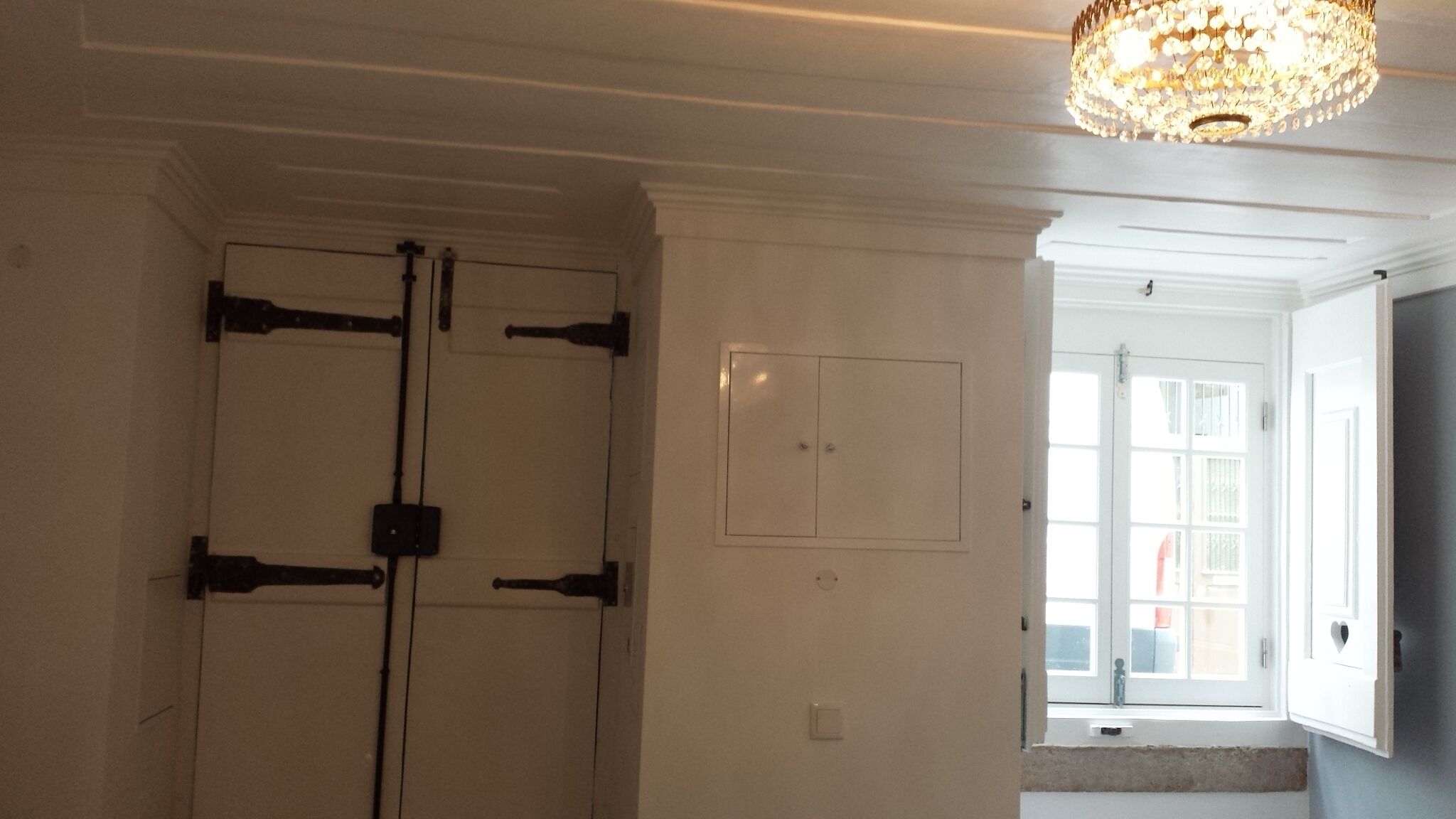 A room with a closed door, a light switch, and a window with a view of the outside.