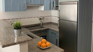 A kitchen with blue cabinets, a stainless steel refrigerator, a microwave, and a granite countertop.