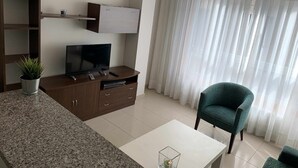 A modern living room with a flat-screen TV on a wooden cabinet, a potted plant, a green armchair, and a white coffee table.
