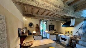 Une cuisine rustique avec des poutres apparentes, un îlot central en bois avec des tabourets, une cuisinière à gaz et un luminaire suspendu.