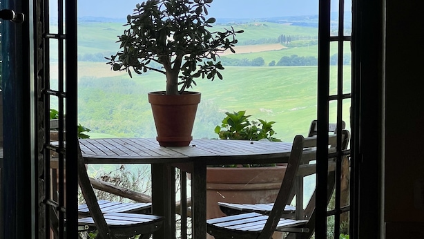 Un balcon avec une table et des chaises, un pot de fleurs et une vue sur un paysage verdoyant.
