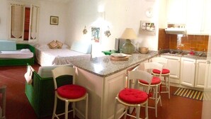 Eine kompakte Küche mit Bar, ein Bett mit grünem Gestell und eine kleine Essecke mit weißen Stühlen.