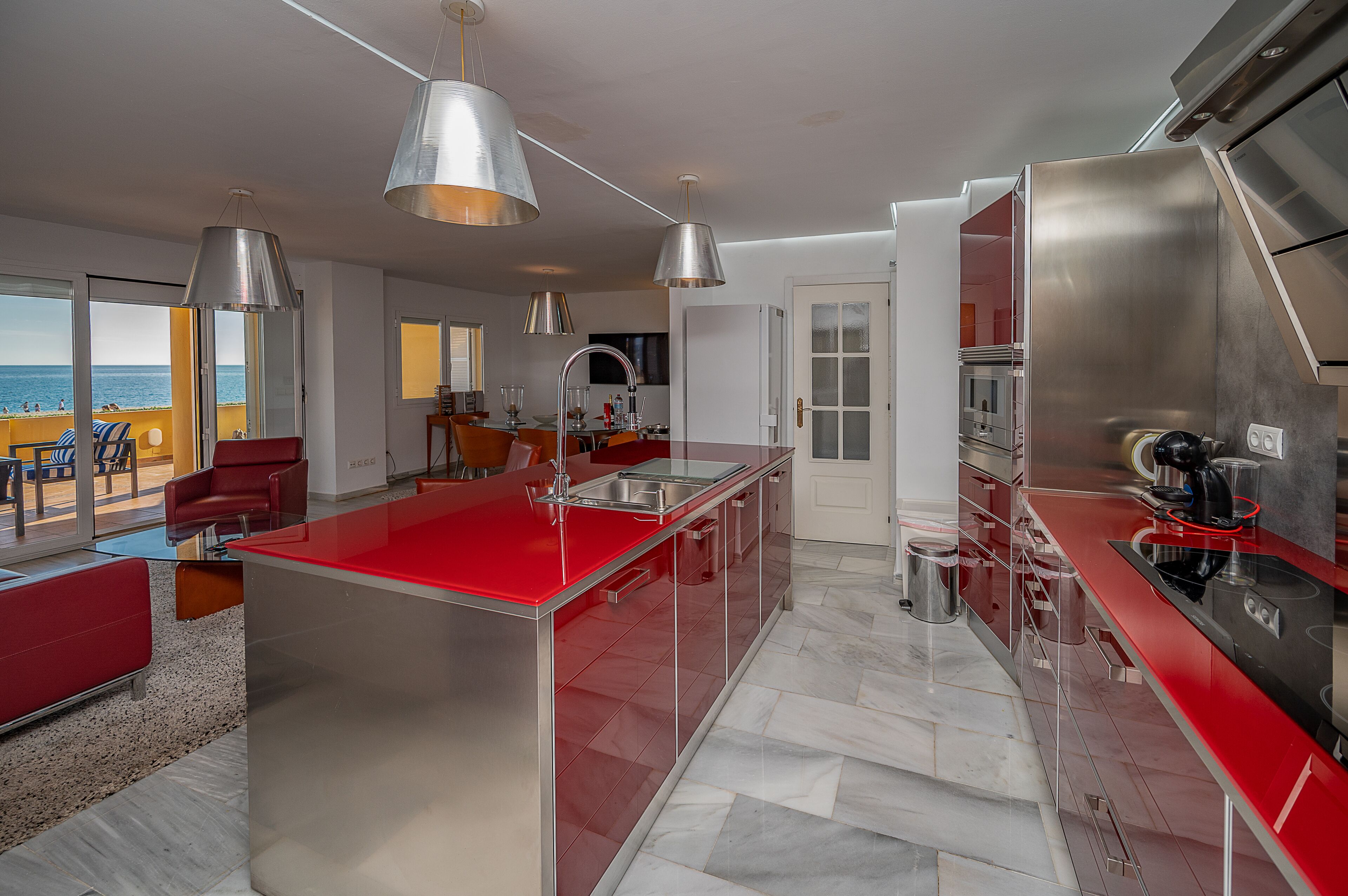 A modern kitchen with red countertops, stainless steel appliances, and pendant lighting.