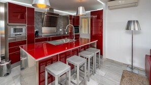 A modern kitchen with red cabinetry, stainless steel appliances, and bar stools.
