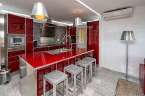 A modern kitchen with red cabinetry, stainless steel appliances, and bar stools.