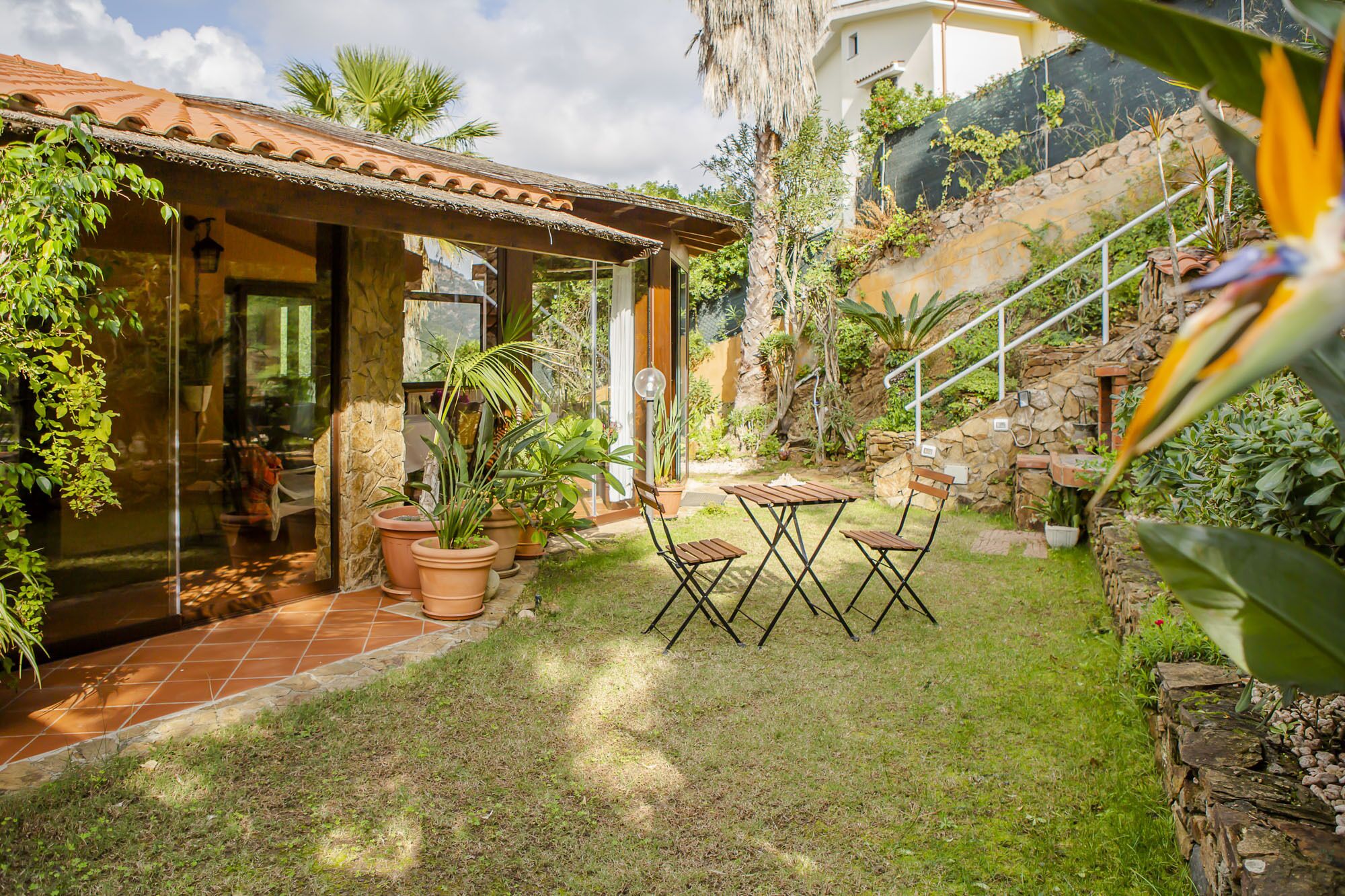 A patio with a table and chairs, surrounded by potted plants and a stone wall.