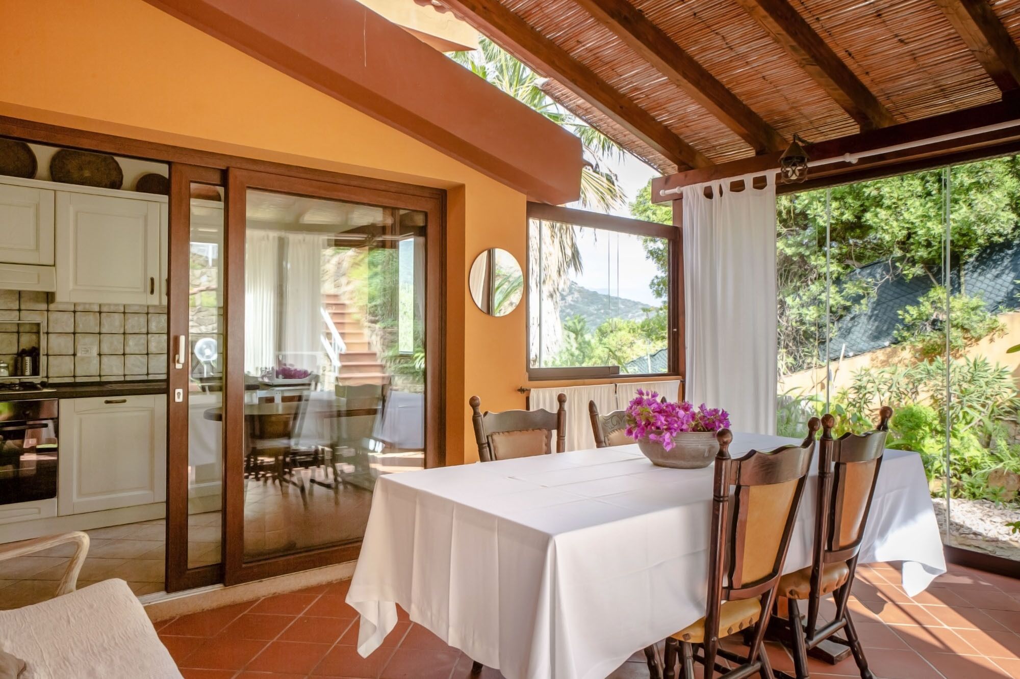 A dining area with a table set for four, a kitchen visible through a glass door, and a view of a mountainous landscape.