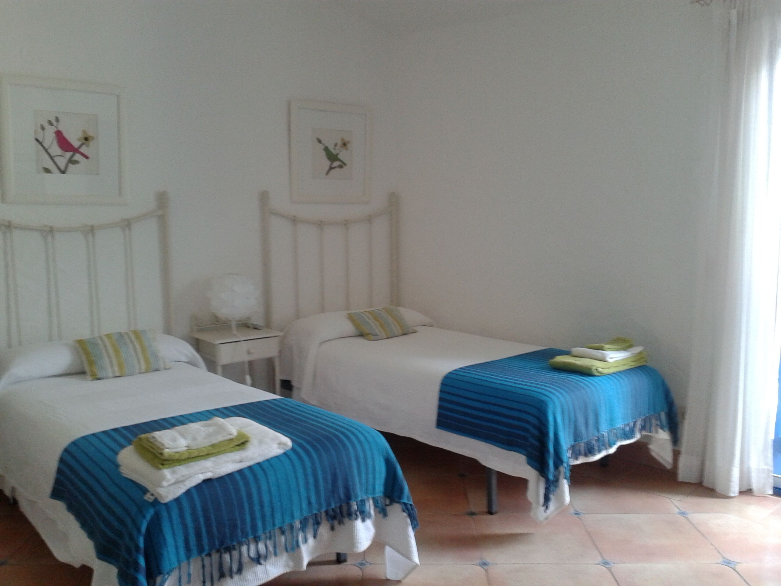 A hotel room with two beds, each with a blue-striped bedspread and pillows. There are framed pictures on the wall above the beds.