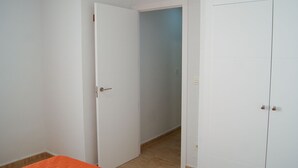 A room with a closed door, a partially open door leading to another room, and a bed with an orange bedspread. - Apartamentos Riviera Beach (Pilar de la Horadada)