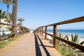 A wooden boardwalk leading to a beach with palm trees and a clear blue sky.