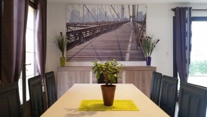 Ein Essbereich mit Tisch, Stühlen, einer Kühlpflanze und einem großen Gemälde einer Brücke.
