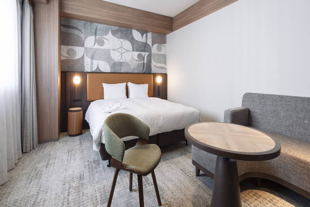 A hotel room with a bed, a chair, a sofa, and a small round table.