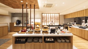 A modern restaurant with a central buffet table, kitchen area, and wooden ceiling.